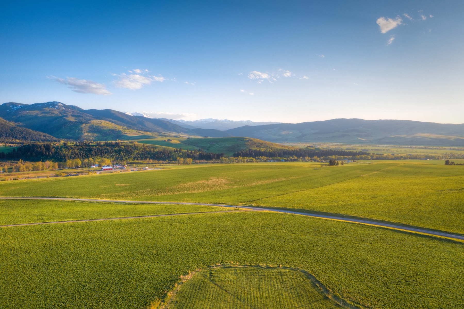 Aerial view of open Gallatin Valley land at sunset with a road crossing green fields below the mountains.